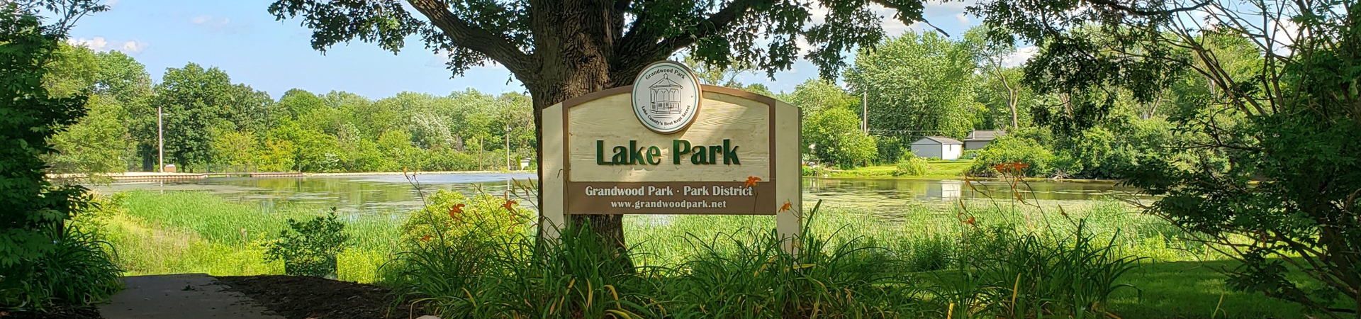 Sign showing name of Lake Park in front of native grasses and pond in summer