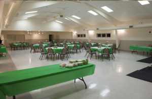 Community center with serving tables and round tables for seating, decorated in green and white