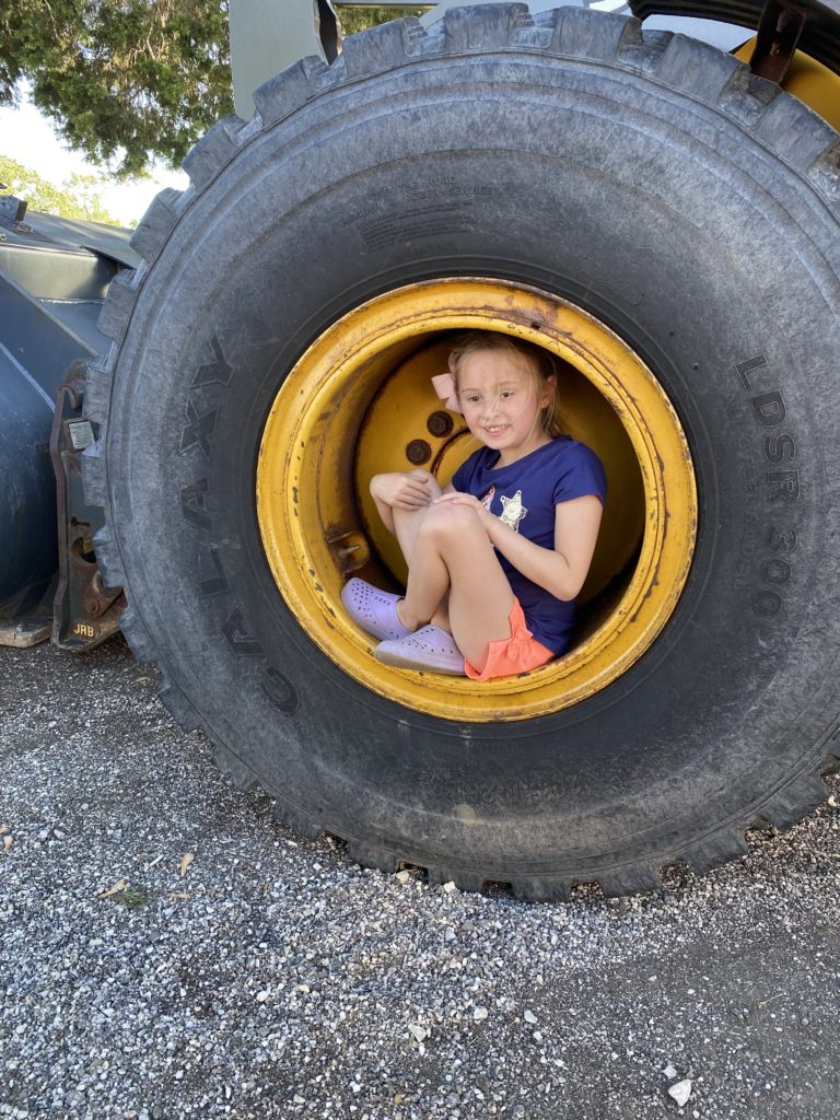 photo of a child sitting inside the wheel of a truck