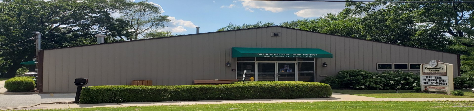 picture of gray community center building with bushes and a sign out front