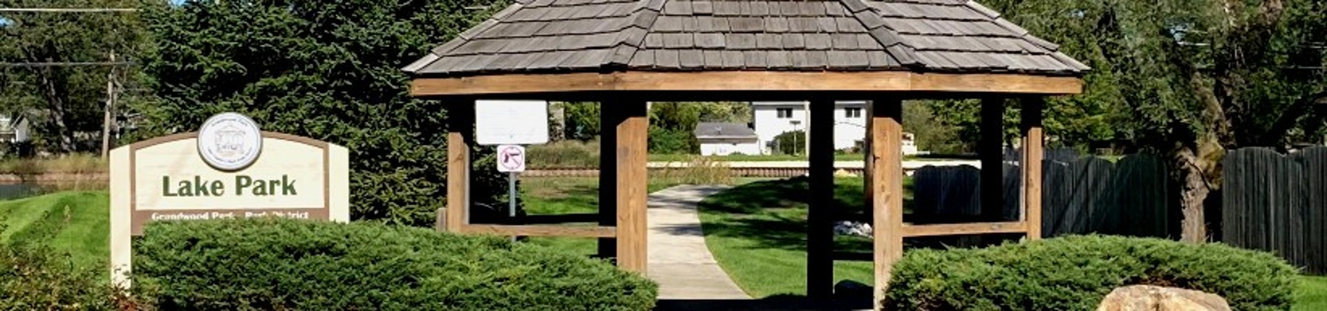 photo of entrance to park with a round gazebo surrounded by bushes and a sign hat says Lake Park