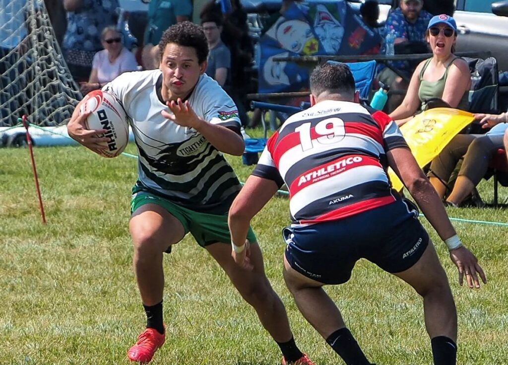 picture of two rugby players, one with a rugby ball, and one trying to block him