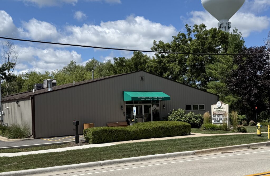 front of community center building with bushes plants and a sign