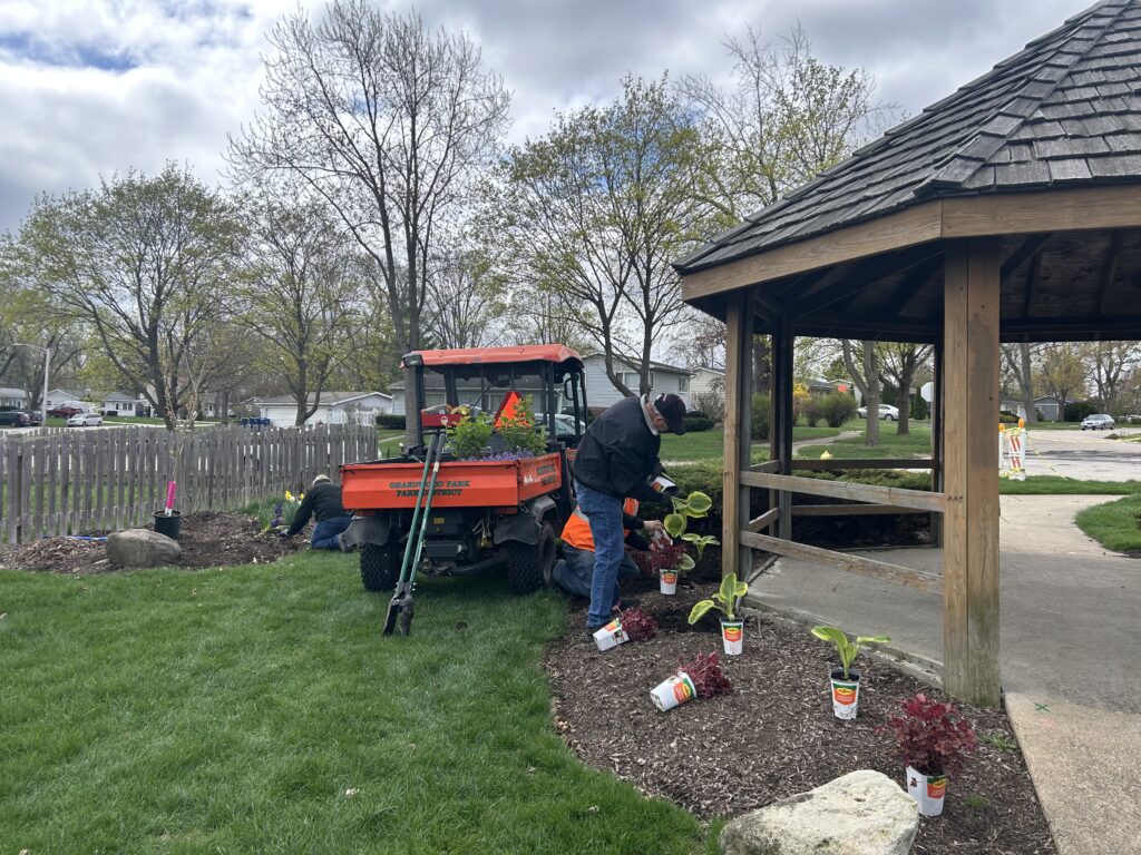 people working around the outside of a wooden gazebo, planting plants